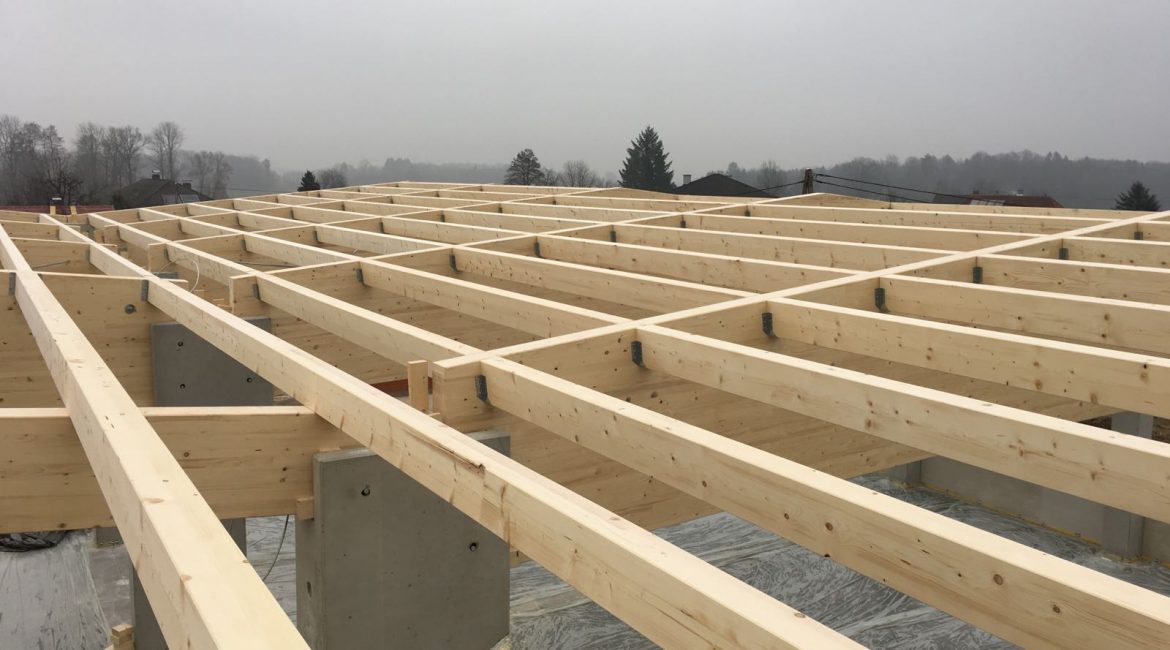 Detailbild einer im Bau befindlichen Halle mit Holz-Dachkonstruktion und Betonstützen.